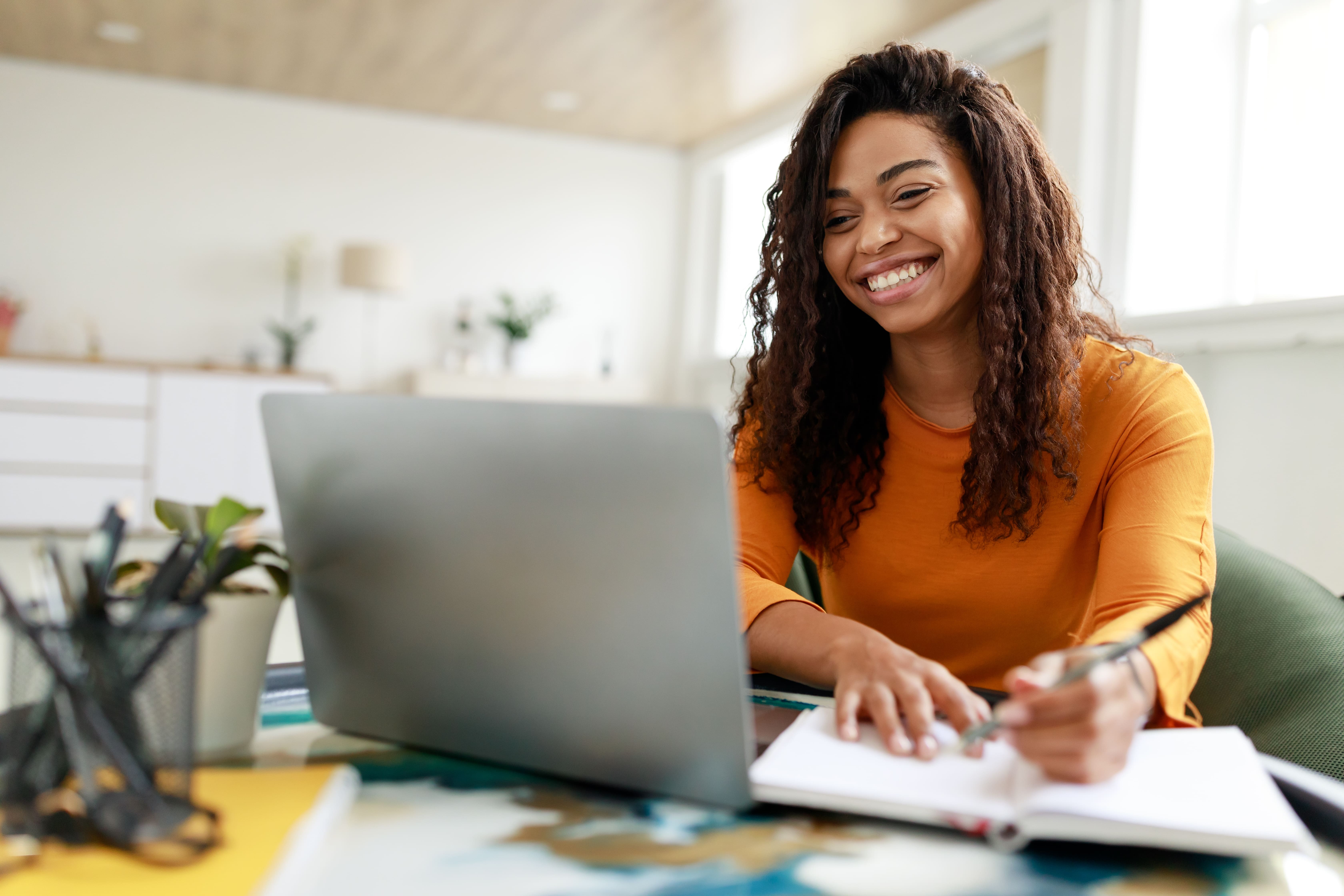 jovem-de-laranja-sorrindo-em-frente-ao-notebook-fazendo-anotacoes